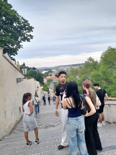 Gruppengespräch auf einer Treppe mit Blick auf die Landschaft, umgeben von grünen Bäumen und einem bewölkten Himmel.